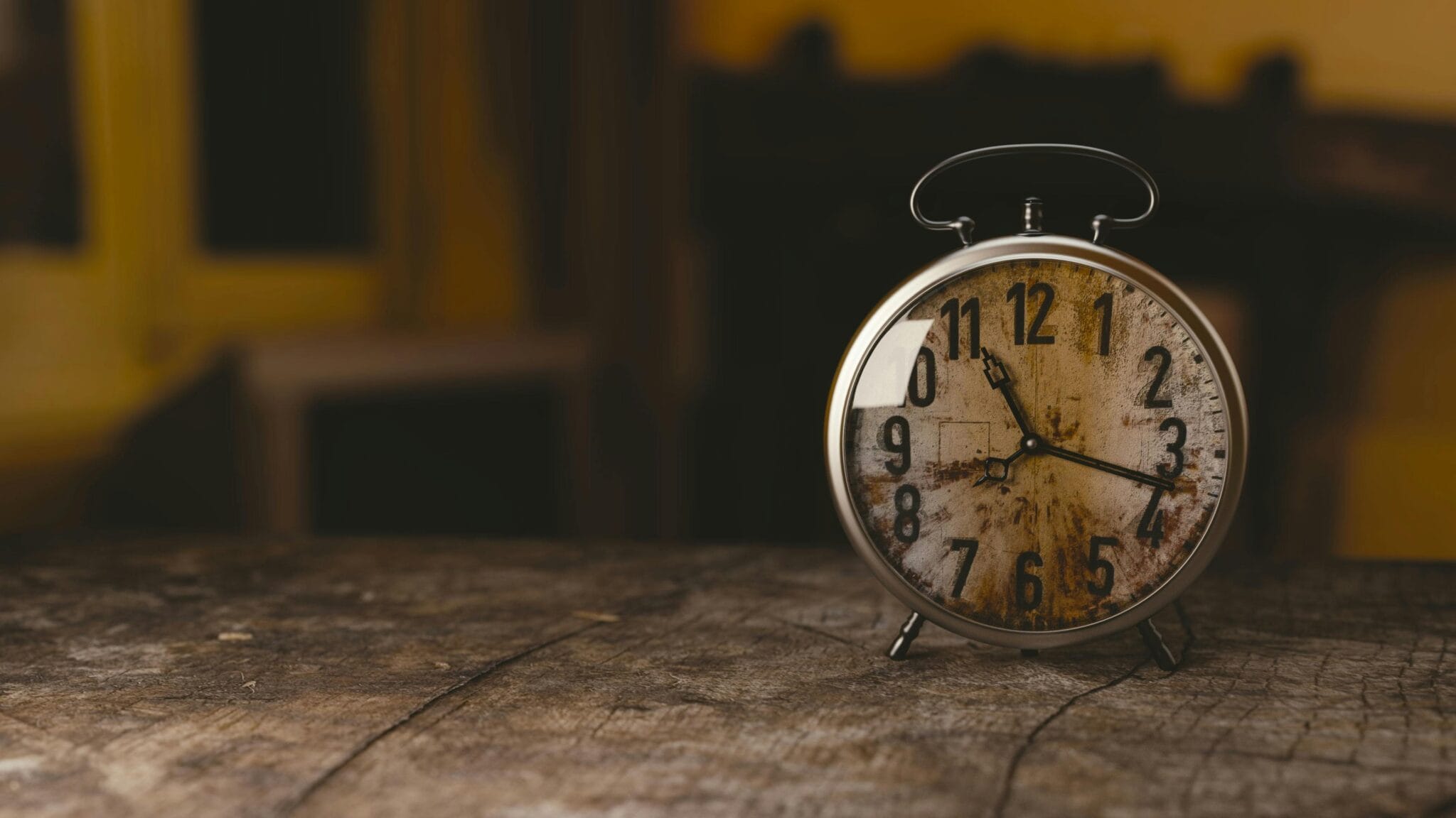 A classic vintage alarm clock sits on a rustic wooden table indoors.
