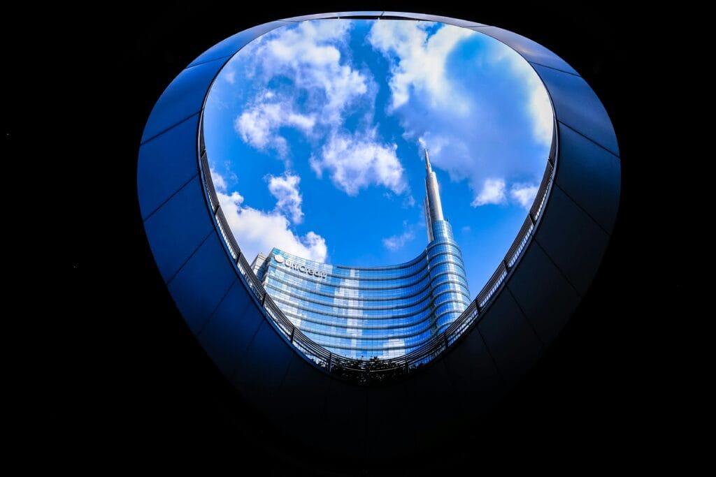 A modern skyscraper reflecting clouds, viewed through a circular architectural frame.